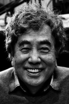 A black and white portrait of Yū Koyama, the creator featured in this Azumi manga review. He is shown from the chest up, wearing a dark jacket over a light shirt, looking directly at the camera with a calm expression.